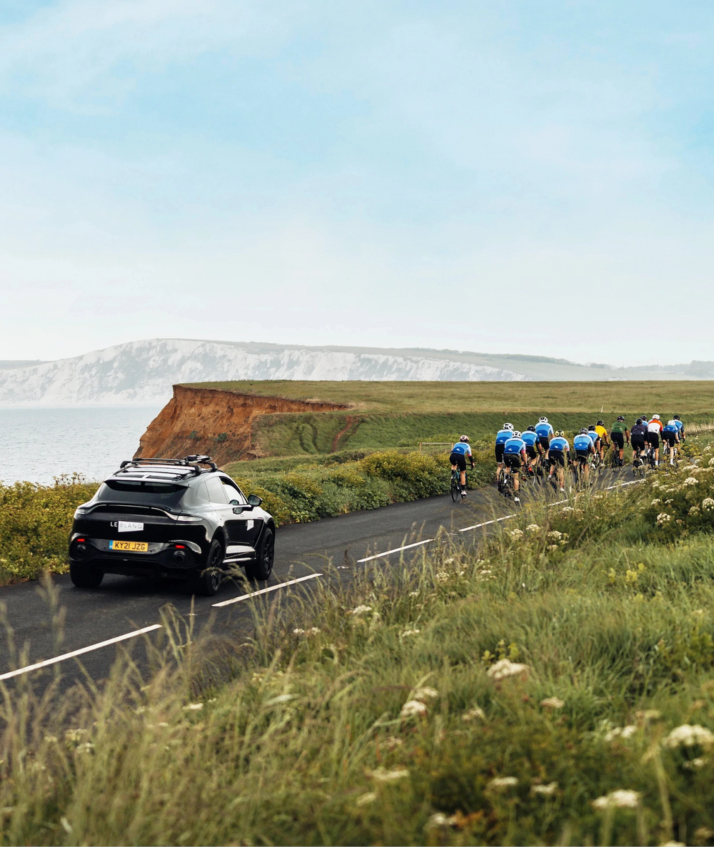 Car following a group of cyclists on a coastal road with cliffs in the background