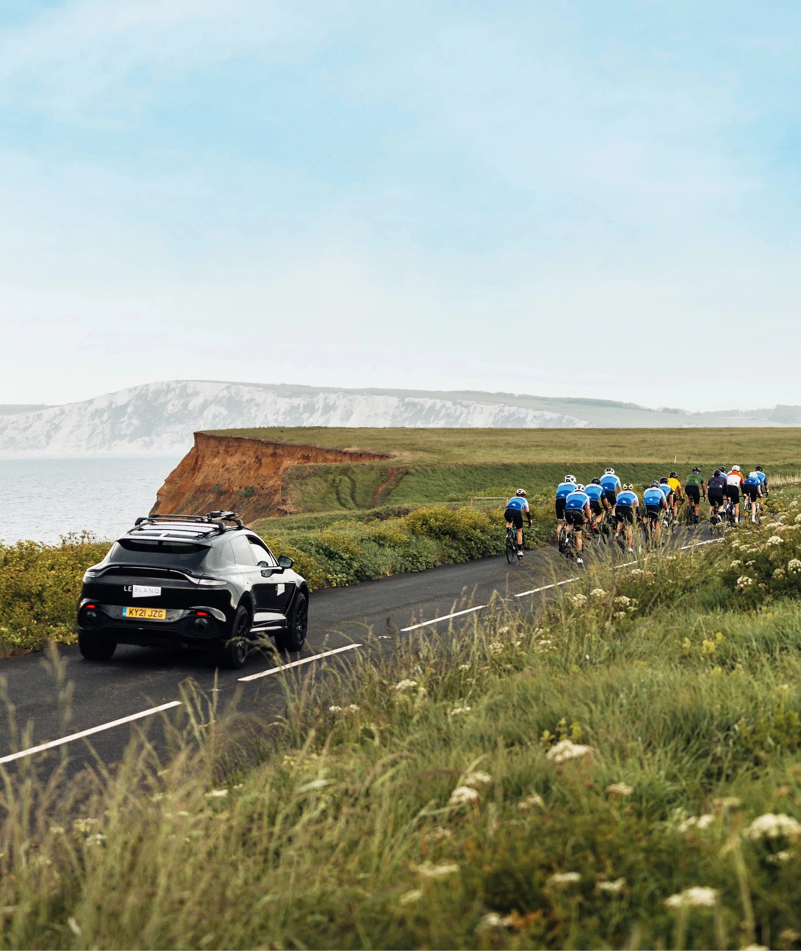 Car following a group of cyclists on a coastal road with cliffs in the background